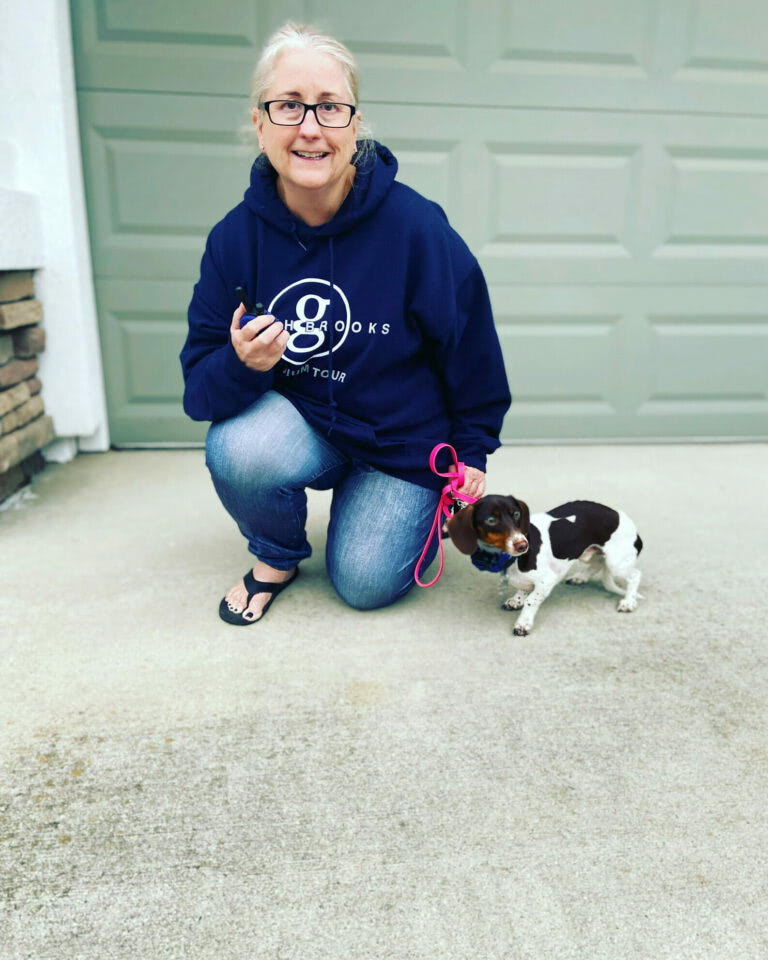 Woman kneels with dachshund on leash.