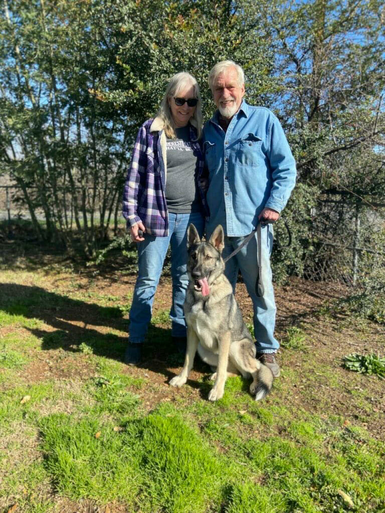 Two smiling owners holding the leash of a calm, seated dog.