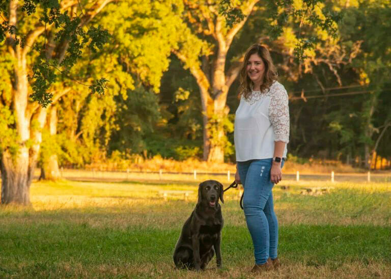 Trisha standing in a grassy field holding the leash of a dog.